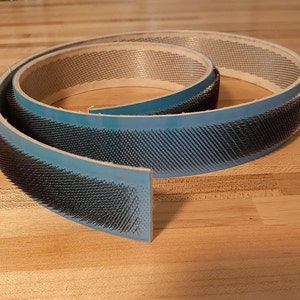 May include: A blue and white fabric belt with black bristles on one side. The belt is rolled up and the bristles are facing out.