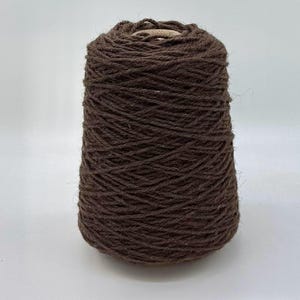 May include: A cone of dark brown yarn, tightly wound and textured. The yarn is a solid, earthy tone, suitable for various crafting projects. The cone shape is clearly defined against a plain white background.