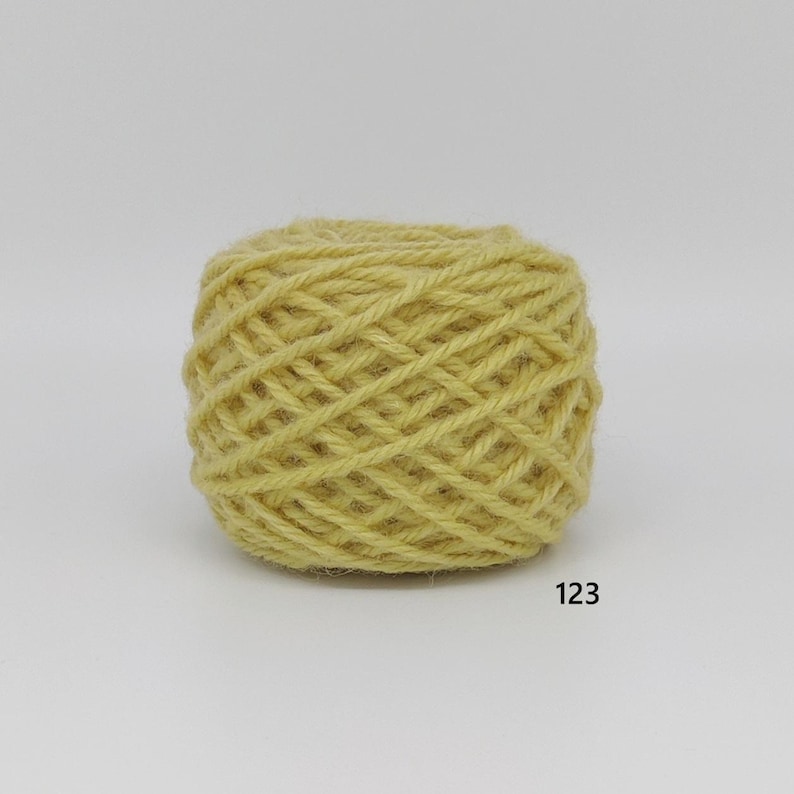 May include: A ball of yellow yarn, tightly wound, with a textured surface. The yarn is a light, muted yellow colour. The number "123" is printed in black on the bottom right.