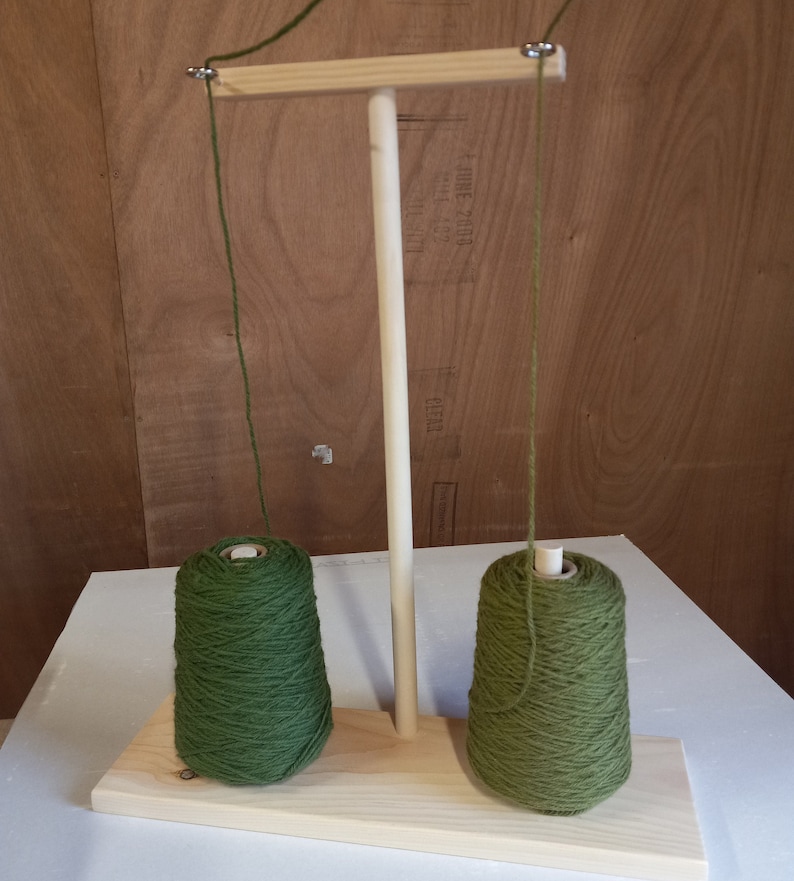 May include: A wooden yarn holder with two spools of green yarn. The yarn holder has a wooden dowel and a crossbar with two hooks.