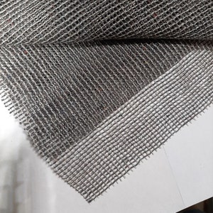 May include: Close-up of a gray and white woven mesh fabric with a textured surface. The fabric has a slightly raised edge.