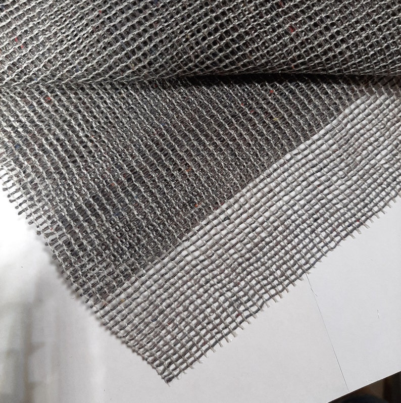 May include: Close-up of a gray and white woven mesh fabric with a textured surface. The fabric has a slightly raised edge.