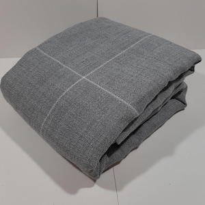 Peut inclure: Tissu gris plié avec un motif quadrillé de lignes blanches. Le tissu est de couleur gris moyen et semble être un matériau tissé. Les bords pliés créent un effet de superposition, suggérant une couverture ou un textile.