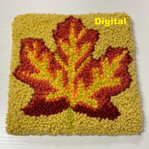 Peut inclure: Un gros plan sur un tapis en laine coloré cousu à la main représentant une grande feuille d'automne stylisée dans des tons de rouge, d'orange et de jaune. La feuille est entourée d'un champ de laine jaune. Le texte "Digital" est visible dans le coin supérieur droit du tapis.