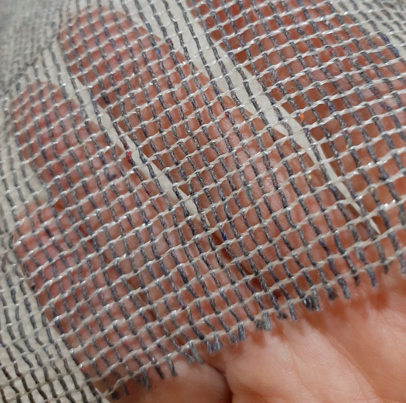 May include: Close-up of a white mesh fabric with a gray woven pattern. The fabric has a slightly frayed edge.