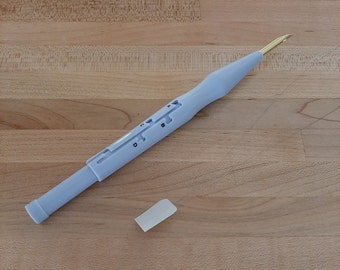 May include: A blue plastic yarn needle with a gold metal tip and a size indicator. The needle is lying on a wooden surface.