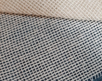 May include: Close-up of two layers of mesh fabric. The top layer is a cream color, rolled over to reveal a layer of dark blue mesh fabric underneath. The mesh has a square grid pattern.
