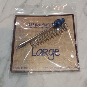 May include: A silver Ultra Punch needle tool with a blue plastic handle and a spring. The packaging says "Ultra Punch The Precision Adjustable" and "Large". It also says "Made in the USA" and "www.ultrapunchneedle.com".