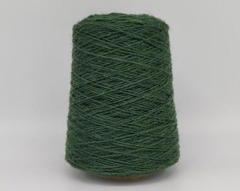 May include: A dark green yarn cone, tightly wound with visible texture. The cone is a deep forest green color, ideal for knitting or crocheting projects. The yarn is on a brown base.