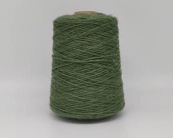 May include: A spool of olive green yarn. The yarn is tightly wound around a cardboard core, forming a conical shape. The yarn has a slightly textured appearance, suggesting a natural fiber. The background is plain white.