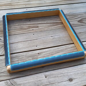 May include: A wooden frame with a blue and gray fabric border. The frame is empty and ready for a canvas.