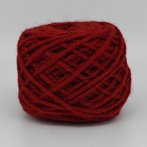 Peut inclure: Une pelote de laine rouge foncé, bien enroulée et texturée. La laine semble être d'une teinte rouge riche, adaptée aux projets de tricot ou de crochet. L'arrière-plan est blanc.