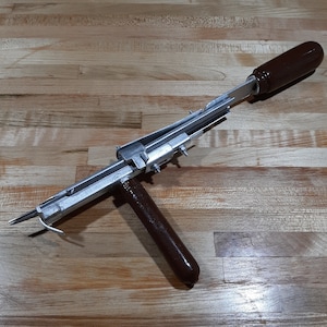 May include: A silver and brown tool with a wooden handle and a metal blade. The tool is used for stretching and tightening fabric.