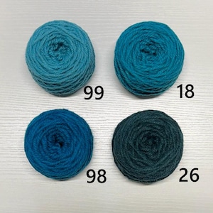 May include: Four balls of yarn in shades of blue and teal are displayed. Each ball has a number printed on it: 99, 18, 98, and 26. The yarn appears to be soft and suitable for knitting or crocheting projects.