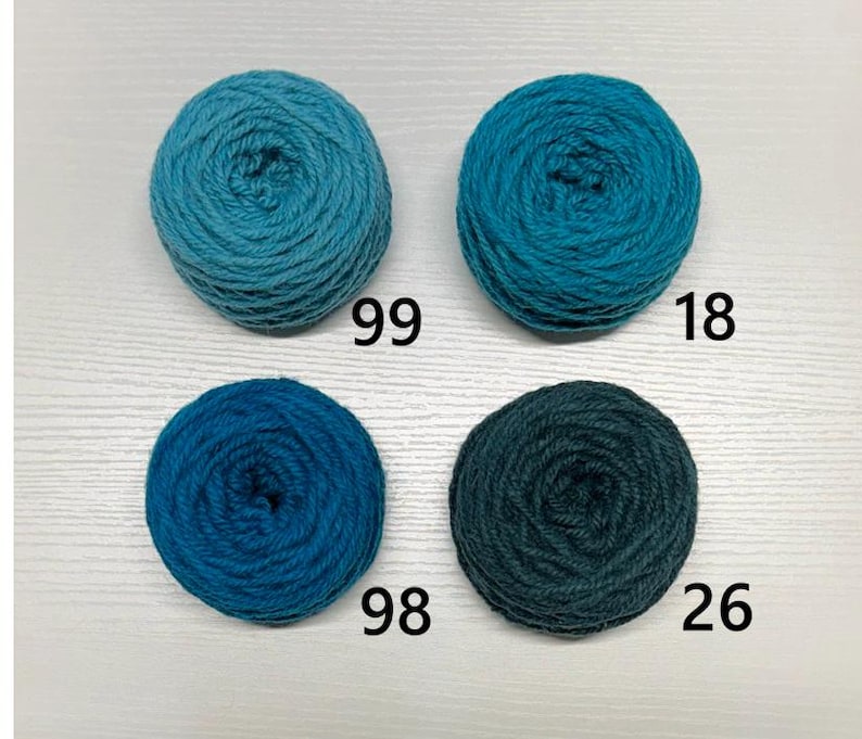 May include: Four balls of yarn in shades of blue and teal are displayed. Each ball has a number printed on it: 99, 18, 98, and 26. The yarn appears to be soft and suitable for knitting or crocheting projects.