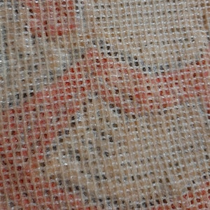 May include: Close-up of a beige mesh fabric with a red and white pattern underneath. The mesh is woven in a square pattern.