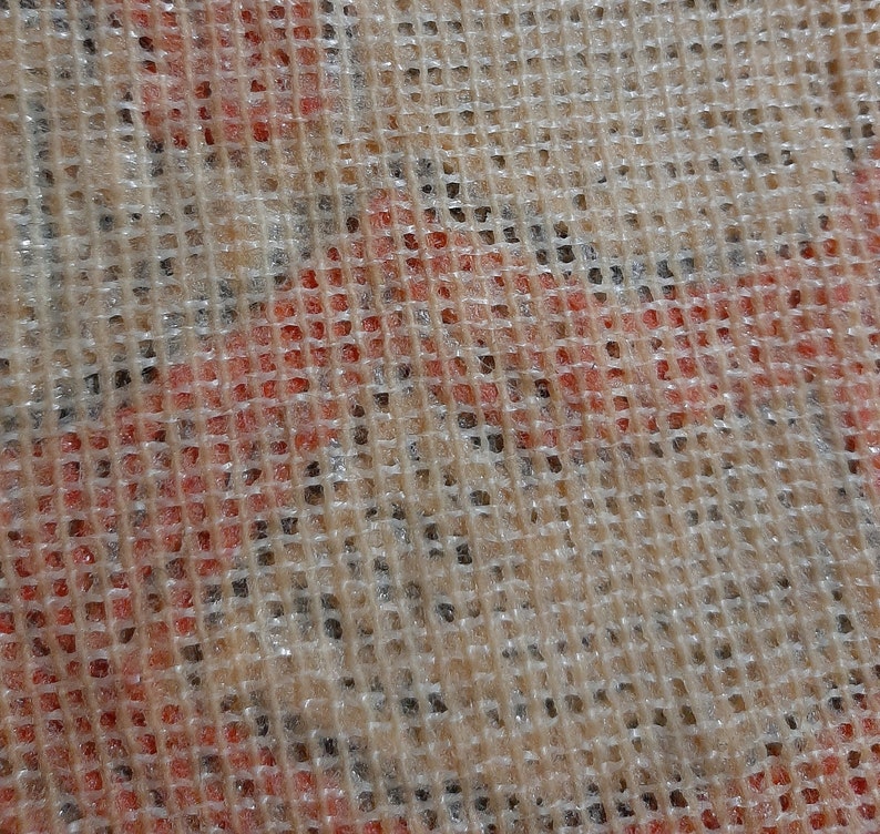 May include: Close-up of a beige mesh fabric with a red and white pattern underneath. The mesh is woven in a square pattern.