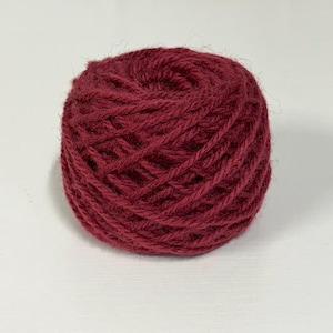May include: A ball of burgundy yarn, tightly wound, sits against a white background. The yarn appears to be a medium weight, suitable for various knitting or crochet projects. The color is a deep, rich red with a slight sheen.