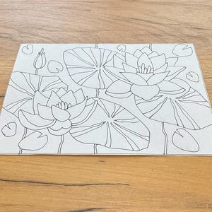 Peut inclure: Un dessin au trait en noir et blanc de nénuphars et de feuilles de nénuphar. L'illustration présente deux fleurs ouvertes, plusieurs feuilles de nénuphar et quelques bourgeons non éclos. L'œuvre est sur une feuille de papier rectangulaire.