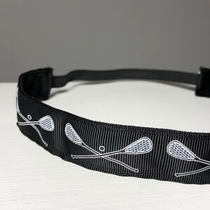 A black nonslip headband with white lacrosse sticks in an X formation.  The lacrosse stick pattern repeats along the length of the headband.  The back of the headband is lined with velvet and there is elastic that is worn toward the back of the head.