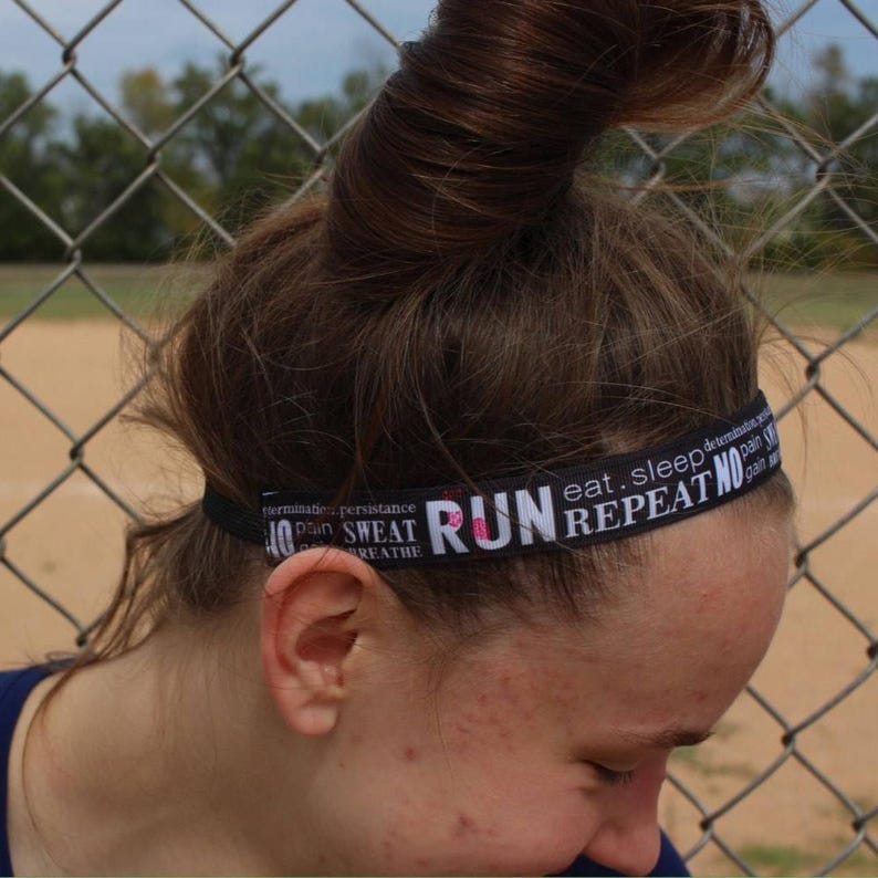A woman with long brown hair is wearing a black headband with the text "run eat sleep repeat no" in white. The headband is worn on her forehead.