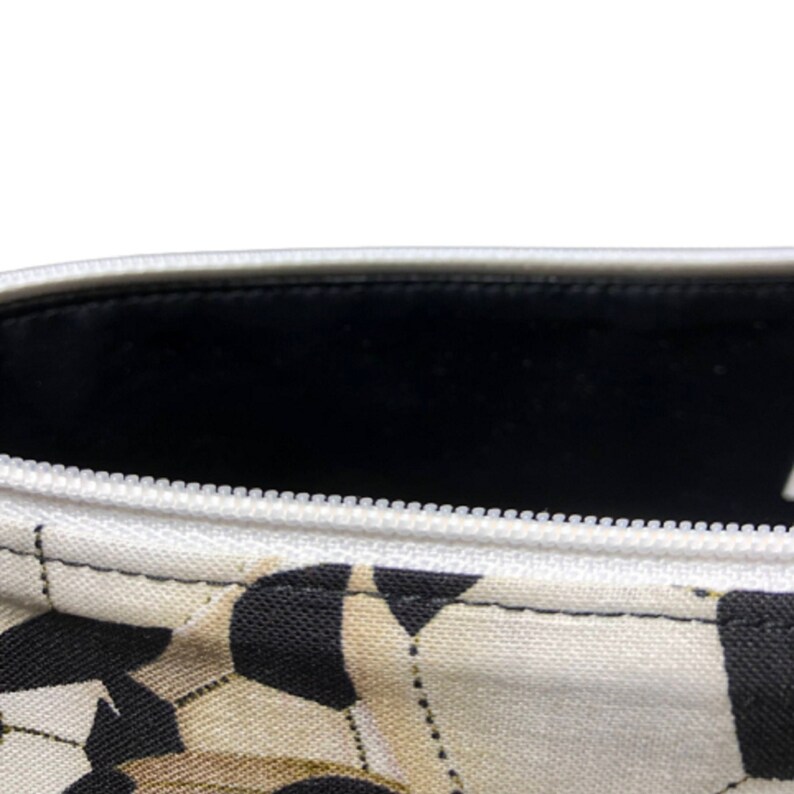 A white zippered pouch with a black and white floral print. The pouch is open and the inside is lined with black fabric.