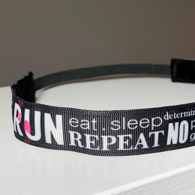 Black headband with white text that reads "RUN eat. sleep determination. pain NO gain repeat".