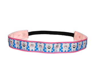 May include: A pink and blue headband with a repeating pattern of white teeth with smiling faces. The headband has a black elastic band and a pink fabric lining.