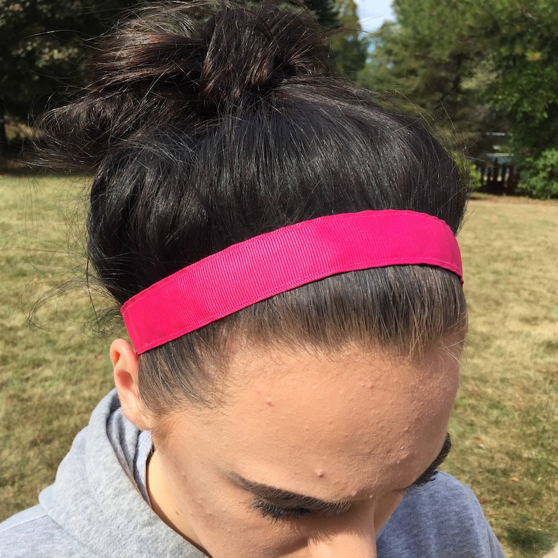 A hot pink headband made of a grosgrain ribbon. The headband is worn by a person with dark hair pulled back in a bun.