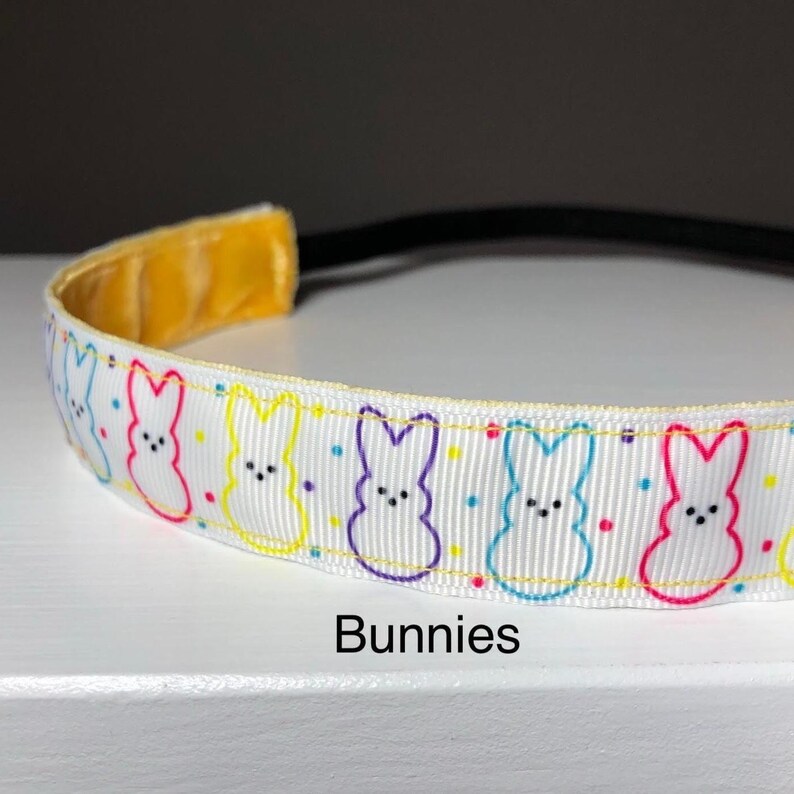 May include: White headband with a repeating pattern of colorful outlined bunnies and white polka dots. The ribbon has the text "Bunnies" printed below it.