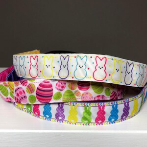 Three colorful headbands with Easter-themed patterns. The top headband features white bunnies with yellow, pink, and blue accents. The middle headband has a white background with pink, yellow, and blue eggs. The bottom headband has a white background with pink, yellow, and purple bunnies.