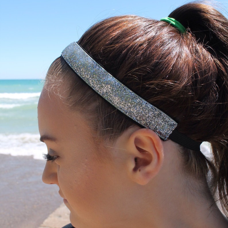 May include: A silver glitter headband with a black elastic band. The headband is worn by a person with brown hair.