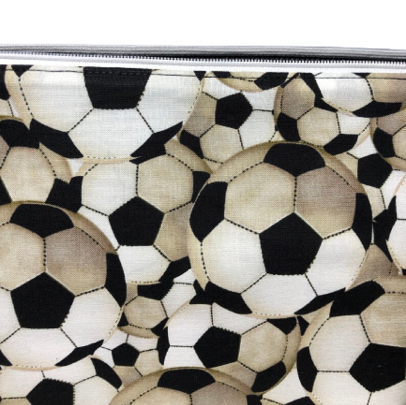 A black and white fabric with a repeating pattern of soccer balls. The soccer balls are beige and white with black stitching.