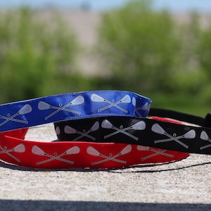 three lacrosse headbands stacked on top of each other.  the nonslip headbands are in blue, black, and red with crossing lacrosse sticks in white on each color option