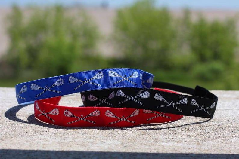 three lacrosse headbands stacked on top of each other.  the nonslip headbands are in blue, black, and red with crossing lacrosse sticks in white on each color option