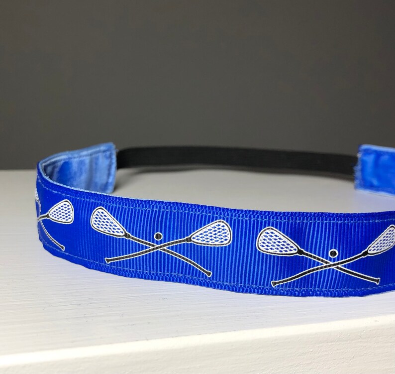 A blue nonslip headband with white lacrosse sticks in an X formation.  The lacrosse stick pattern repeats along the length of the headband.  The back of the headband is lined with velvet and there is elastic that is worn toward the back of the head.