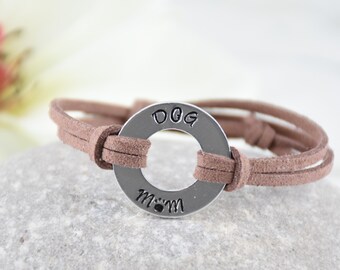 May include: A brown suede bracelet with a silver metal charm that says "DOG MOM" with a paw print symbol.