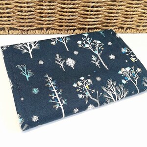 May include: A dark blue fabric with a white and blue winter forest print. The fabric features stylised trees, snowflakes, and geometric shapes.