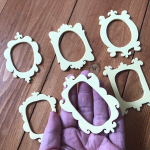 May include: Six small, ornate, yellow picture frames with a scalloped edge. The frames are made of wood and have a vintage look.