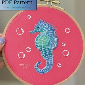 May include: A hand-stitched embroidery hoop featuring a blue and green seahorse on a pink background. White bubbles surround the seahorse. The text "PDF Pattern" and "Stitch Please By Kiki" are visible.
