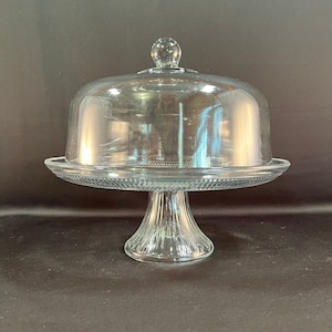 May include: A clear glass cake stand with a dome lid. The stand has a fluted base and a wide, flat top.