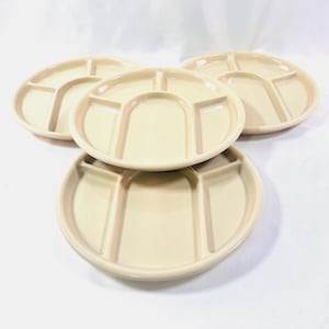 May include: Four beige divided plates. Each plate has a circular shape with five separate compartments. The plates are made of ceramic or a similar material. The plates are stacked and arranged in a group.