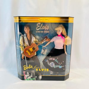 May include: A collector's edition Barbie Loves Elvis gift set featuring a Barbie doll dressed in a pink sweater and black skirt with a musical note design, and an Elvis doll dressed in a gold jacket and holding a guitar. The box features the text "Barbie Loves Elvis" and "Elvis Live On Stage".