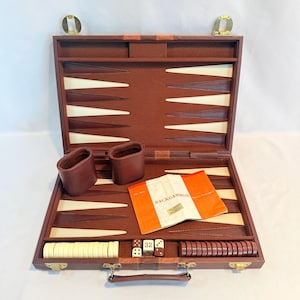 May include: Open brown backgammon set with ivory and brown game pieces, dice, and a booklet. The set includes two brown leather dice cups and a handle for carrying. The game board features a classic design with ivory and brown triangles.