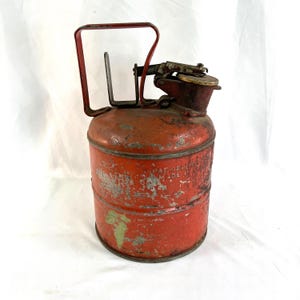 May include: Red metal gas can with a hinged spout and a carrying handle. The can has a label that reads "Pat. Applied For Made in USA".