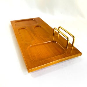 Cómoda de caballero, de madera clara, con barras de latón para billetera o teléfono, cuatro compartimentos para joyas, monedas y llaves.