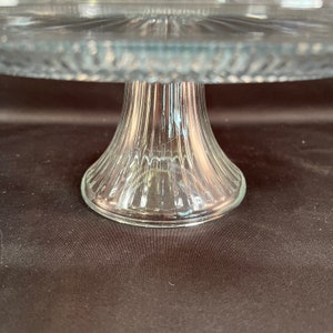 May include: A clear glass cake stand with a fluted base. The stand is designed for serving cakes, pastries, or other desserts.