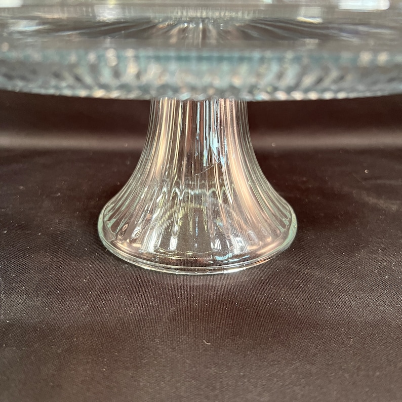 May include: A clear glass cake stand with a fluted base. The stand is designed for serving cakes, pastries, or other desserts.