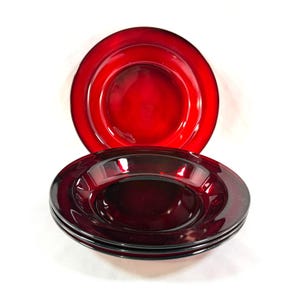 May include: A stack of four deep red glass plates with a glossy finish, and one additional plate. The plates have a simple, elegant design, perfect for serving meals. The plates are a rich, dark red color.