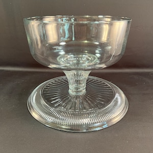 May include: A clear glass pedestal bowl with a fluted base. The bowl is designed for serving desserts or other foods.